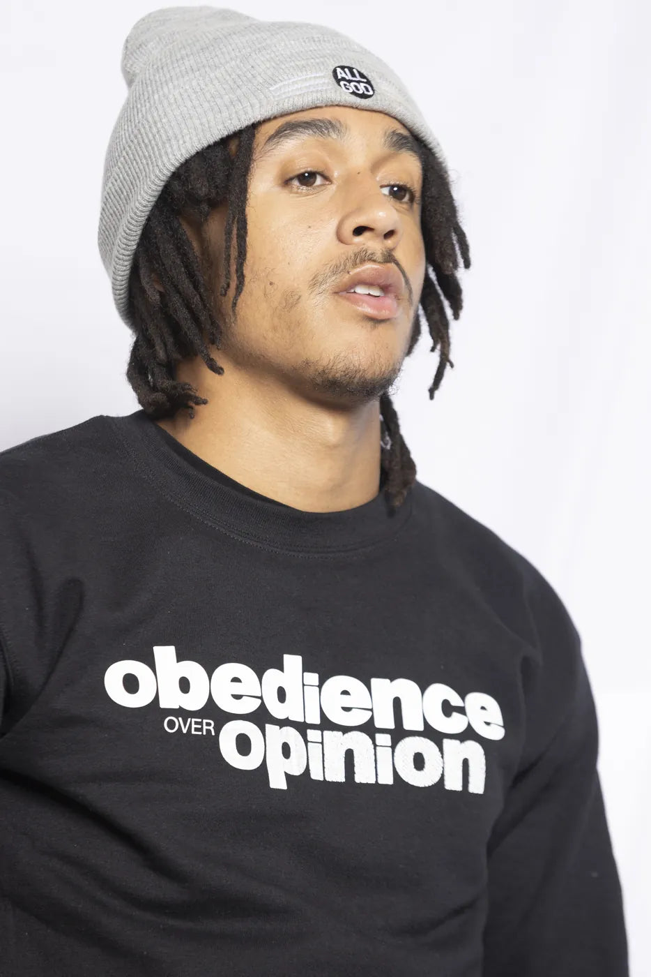 Model in the black Obedience Over Opinion crewneck and grey All God beanie.