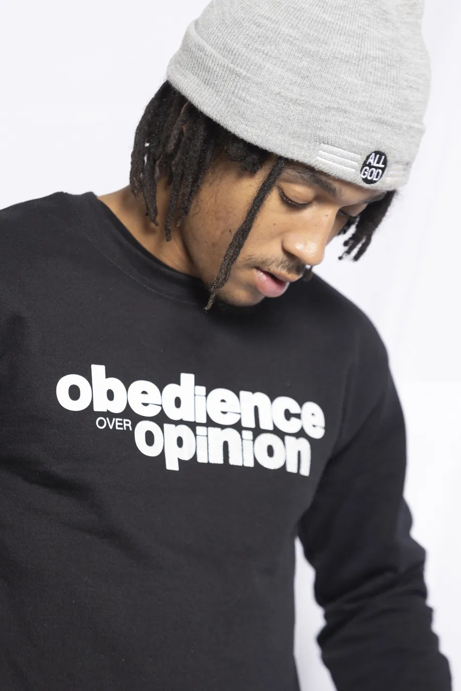 Model in the black crewneck and grey All God beanie, looking down.